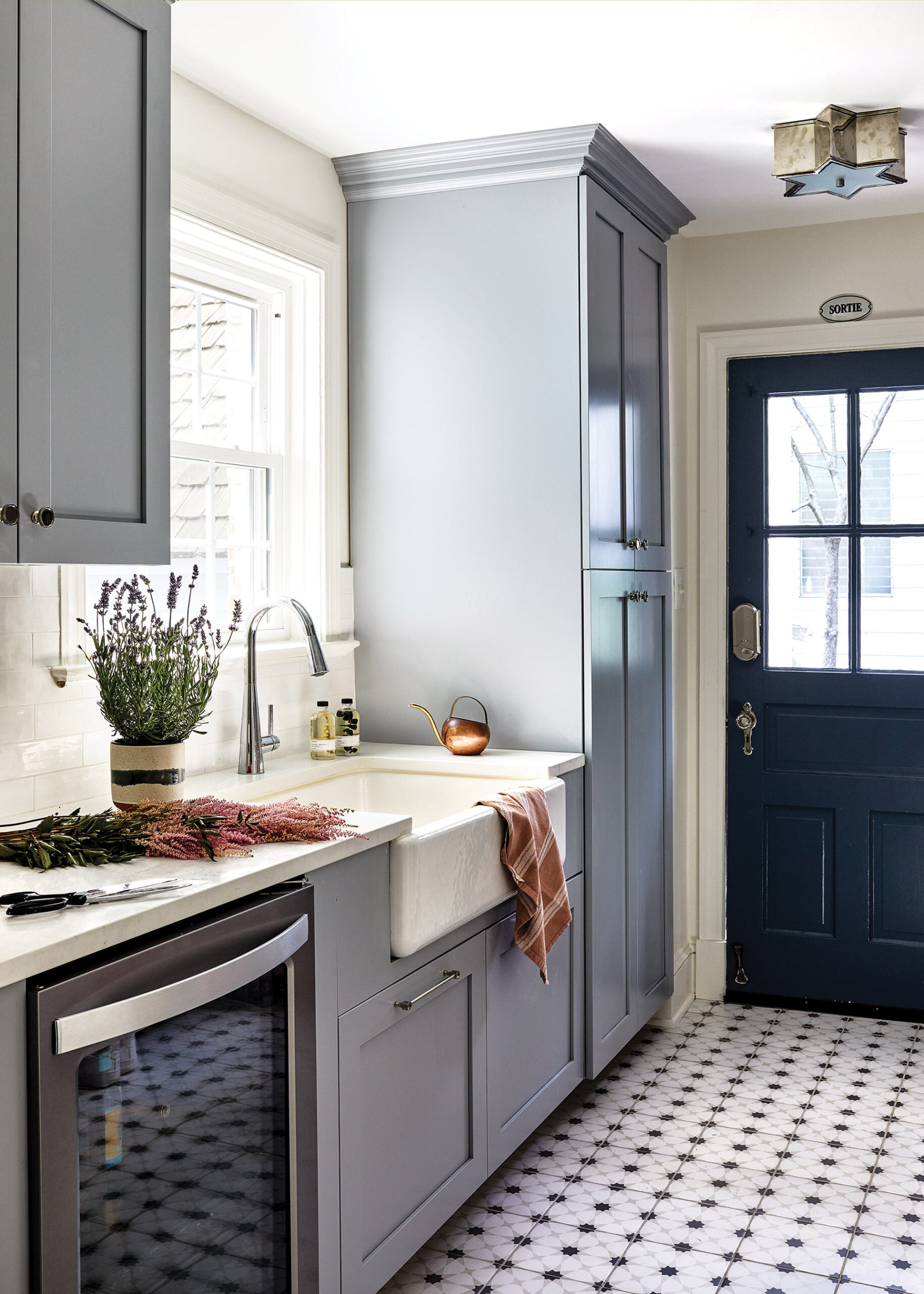 Farmhouse sink in the chic utility room is flanked by a beverage fridge on one side and floor-to-ceiling cabinetry on the other.